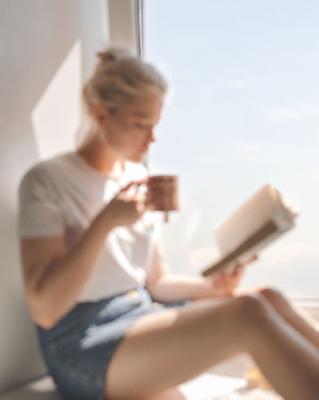 A woman reading with a warm drink in a sunlit room